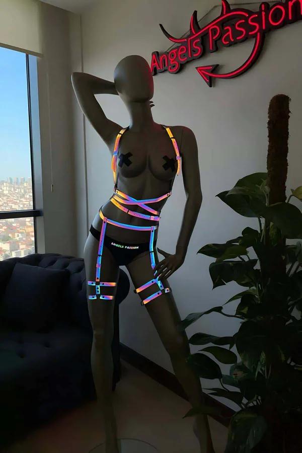 Model wearing black Rainbow Reflective Full Body Harness Set glowing in a brilliant neon spectrum under direct camera flash front view
