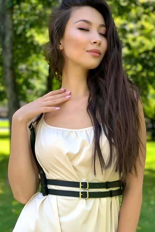 Black faux leather double buckle waist harness with gold-tone hardware and adjustable shoulder straps worn over cream dress