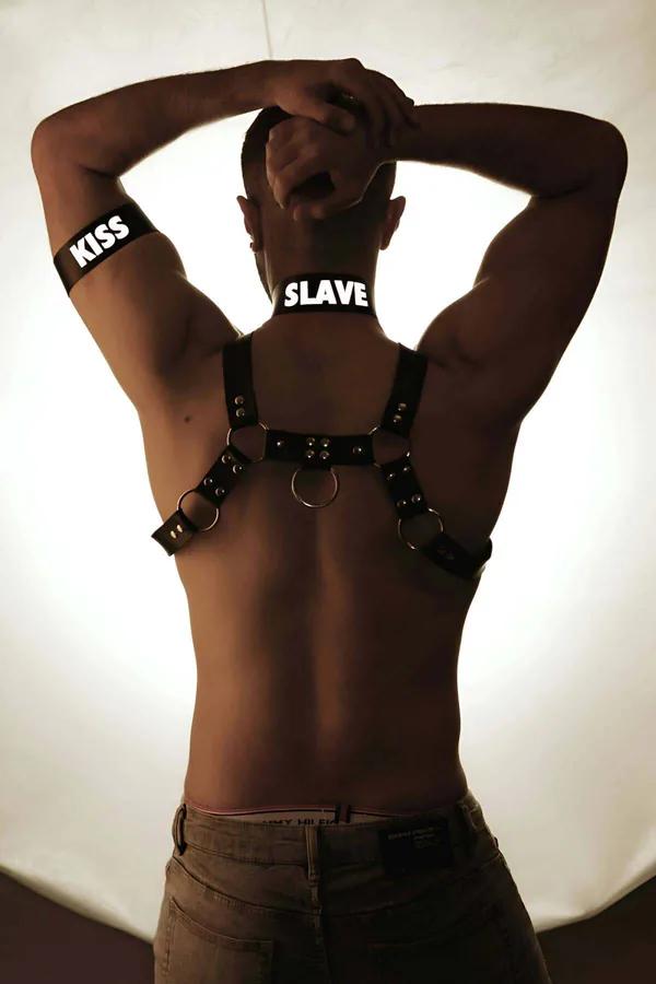 black faux leather chest harness back view with four silver O-rings, reflective collar, and matching armband on male model