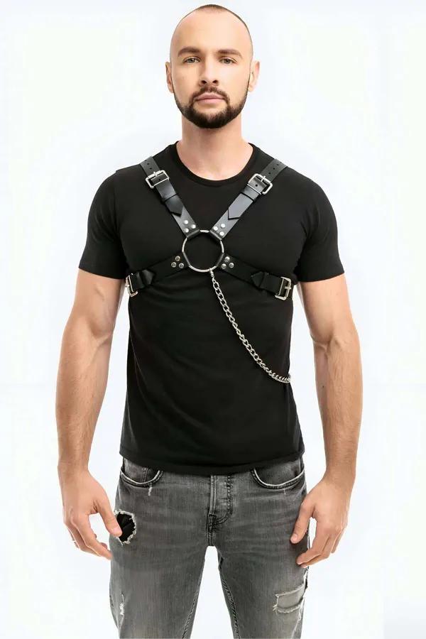 Black faux leather chest harness with silver O-ring and detachable chain link, worn over black t-shirt